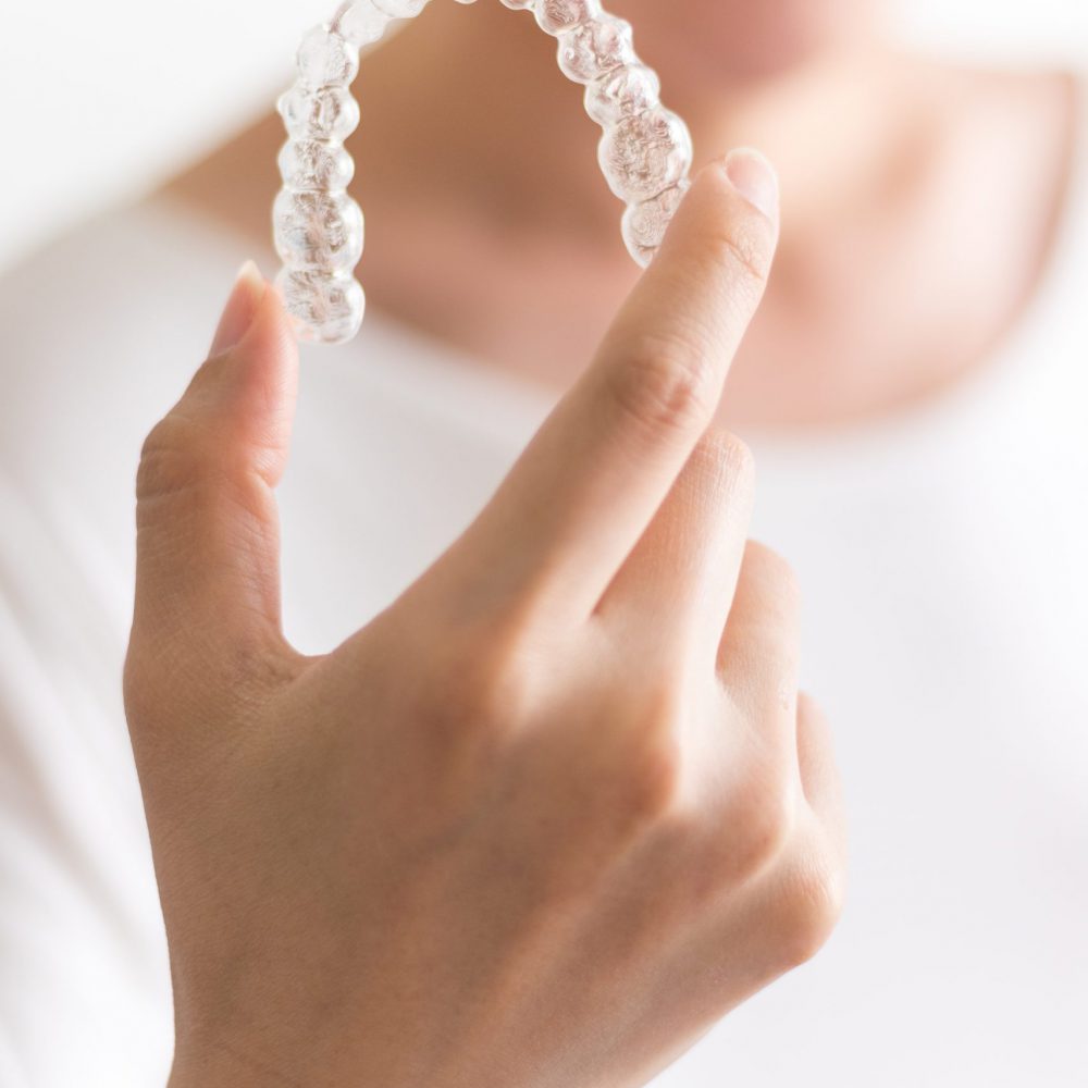 A smiling woman holding invisalign or invisible braces, orthodontic equipment A smiling woman holding invisalign or invisible braces, orthodontic equipment